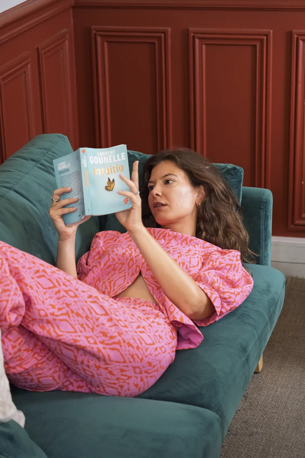 Reading, lying on the green sofa in a patterned pink outfit, portrait session in Paris