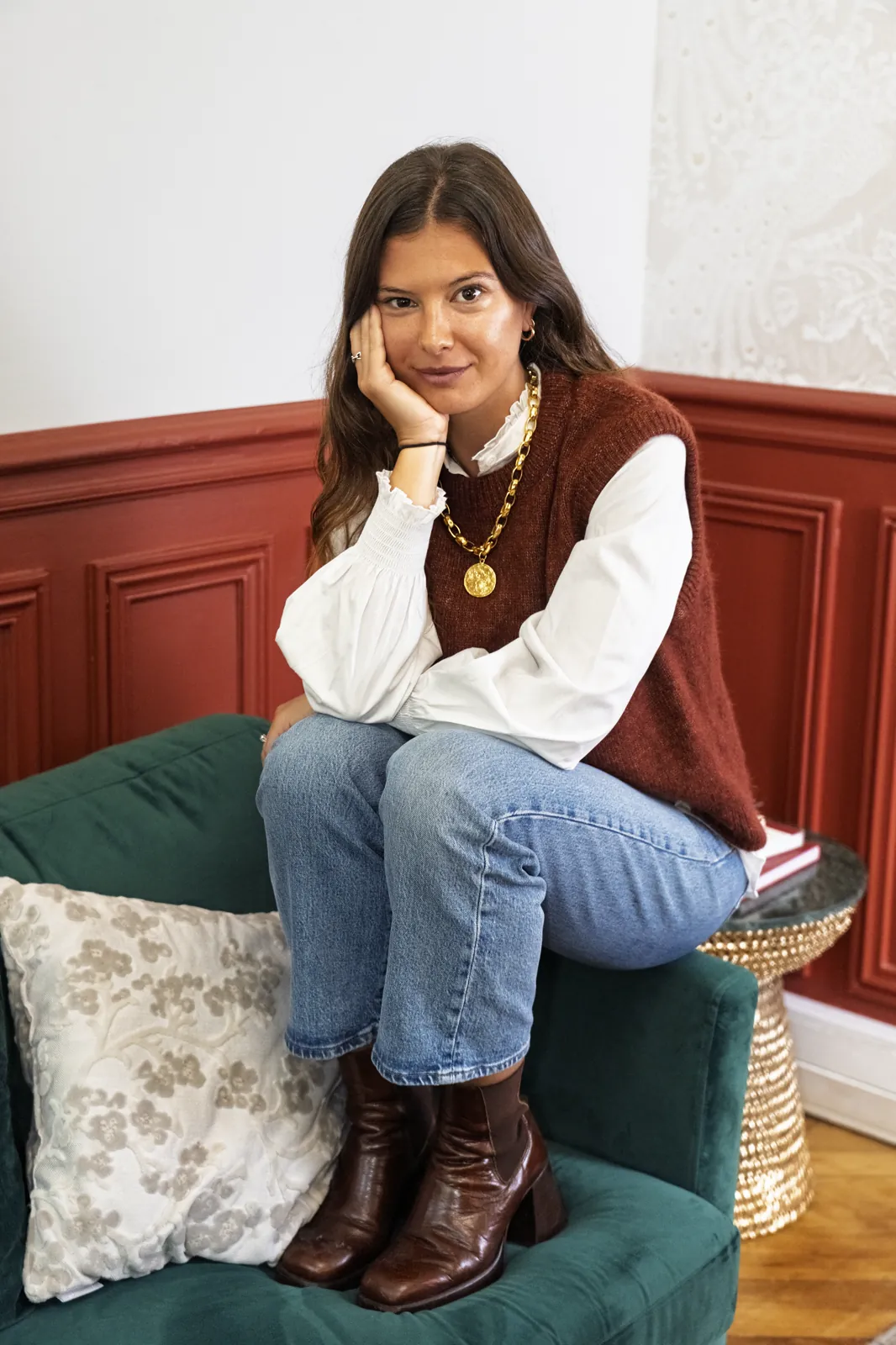Sitting on the armrest, hand against her cheek, looking at the camera