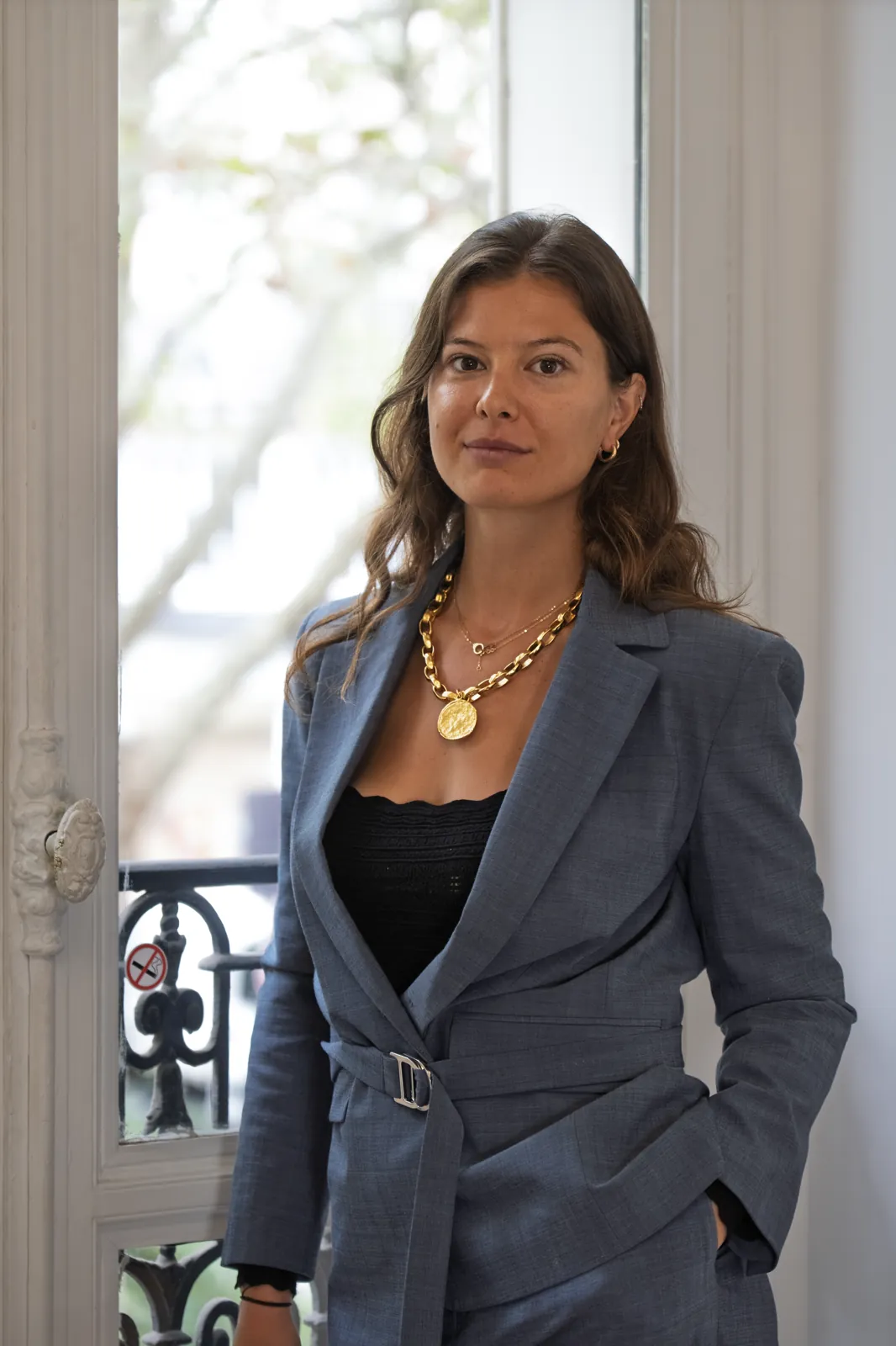 Standing by the window, grey suit, looking at the camera
